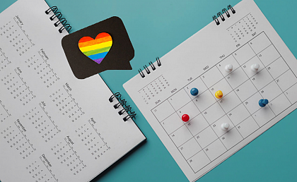 Symbol image: LGBTIQ* events
[Image description: There are two calendars on turquoise background. On the monthly view, several days are marked with colorful pins. Above the calendars is a black speech bubble with a rainbow colored heart.]